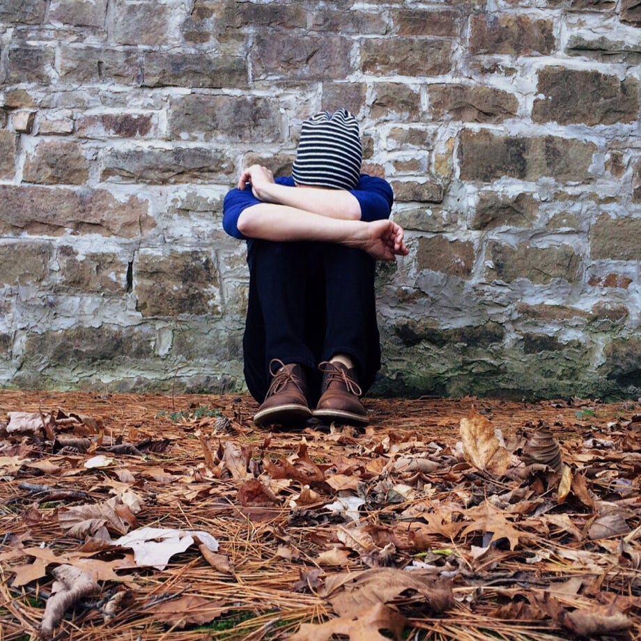 Boy Sitting on Ground Leaning Against Brickstone Wall