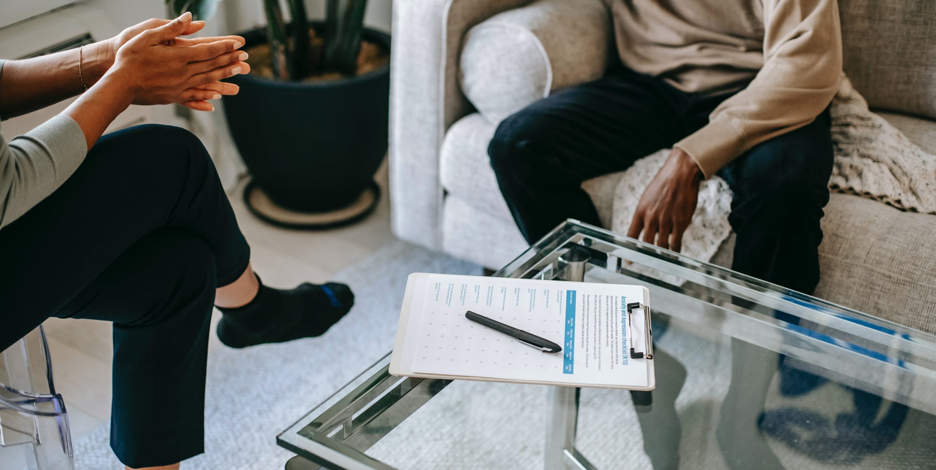 Crop anonymous African American man in casual clothes sitting on sofa and talking to female psychologist during psychotherapy session in modern studio