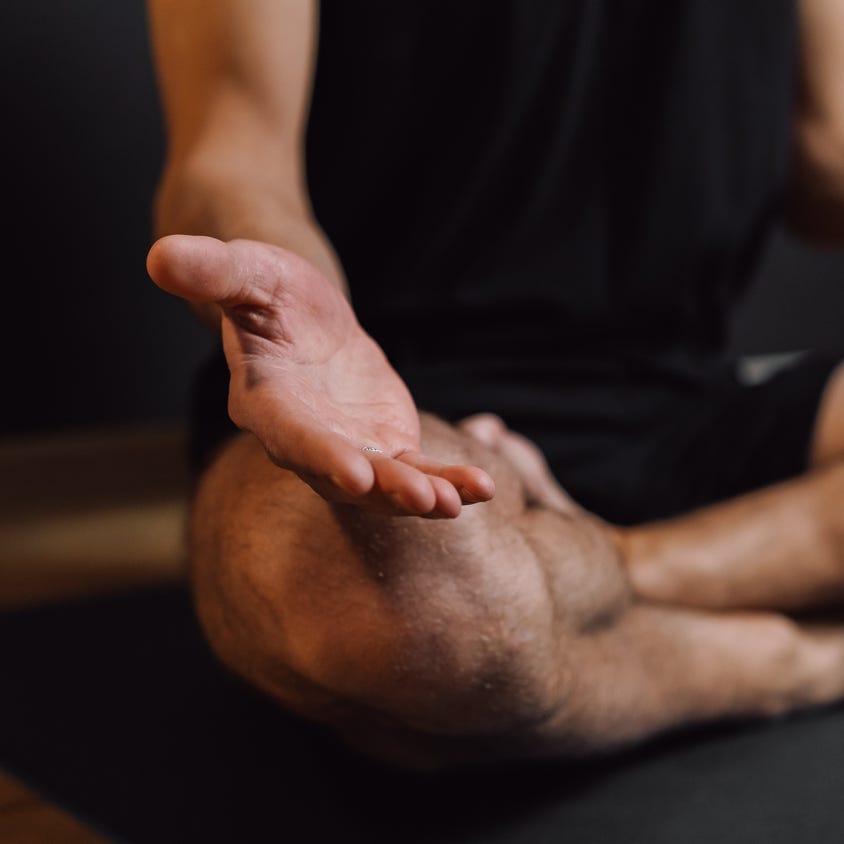 Crop unrecognizable barefoot male sitting with crossed legs on sports mat during stress relief meditation session